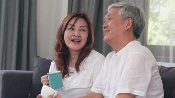 grandparents, husband and wife smile talking and drinking coffee while lying on sofa.