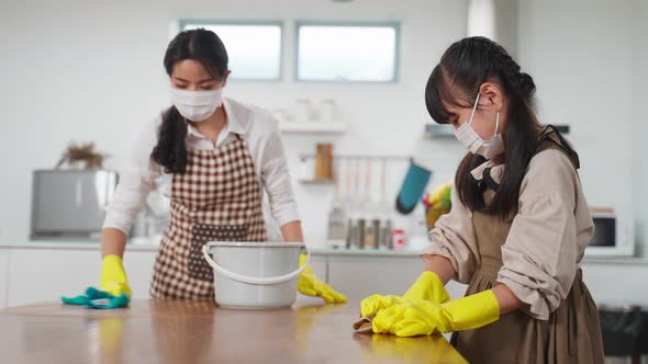 Asian young family parent teaching their kid daughter to clean dining table in kitchen room in house