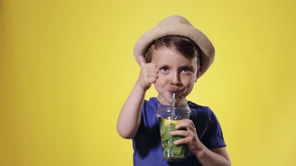 Cute boy Drinking Mojito cocktail From Plastic Cup Over Yellow Studio Background