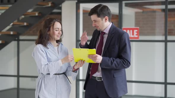 Cheerful Young Beautiful Woman Signing Documents and Receiving Property Key From Man