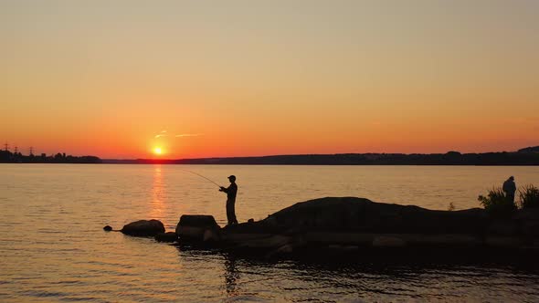 Fishermen on the lake against orange sunset.