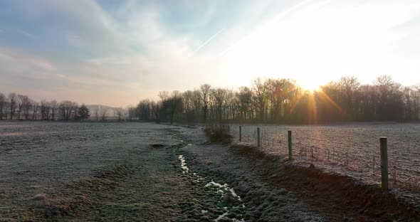 Stream through meadow pasture in winter frost at sunrise. Water reflects sunlight. Soil erosion.