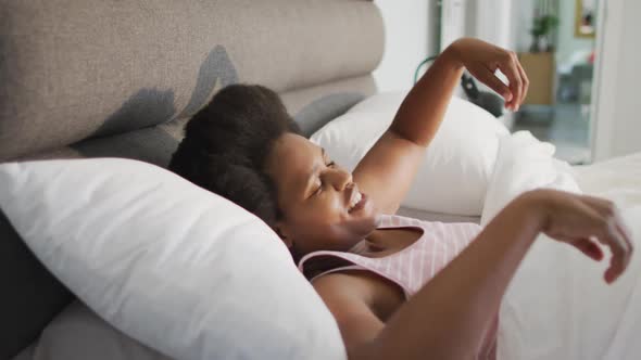 Happy african american woman lying in bed, stretching in bedroom