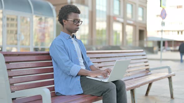 Busy Young African Man Using Laptop Sitting Outdoor on Bench