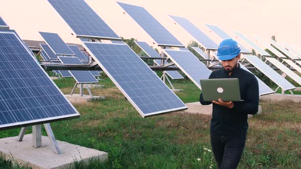Caucasian Industrial Engineer in Uniform Walking Among Solar Panels for Examination.