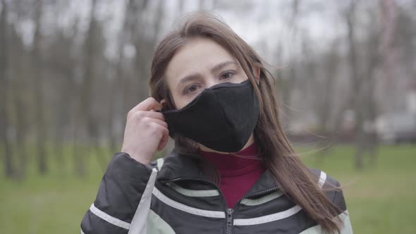 Close-up of Cheerful Young Caucasian Woman Taking Off Face Mask and Smiling at Camera