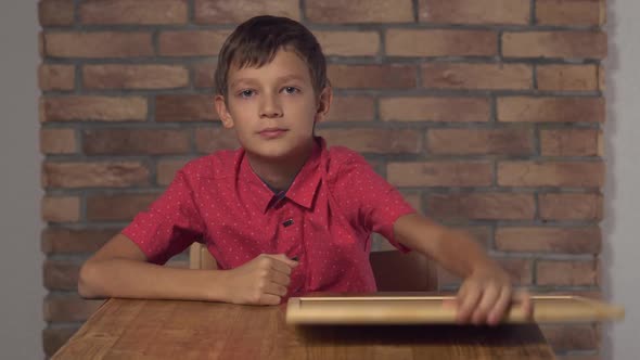 Child Sitting at the Desk Holding Flipchart with Lettering Call Me on the Background Red Brick Wall