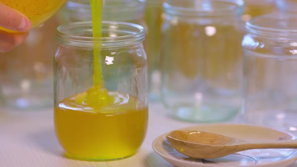 Woman Pours Honey Into Transparent Jars on a White Table