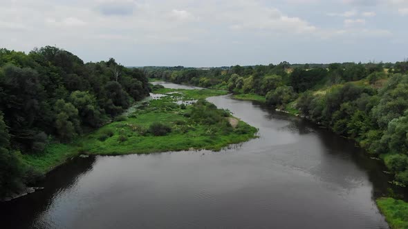 Aerial View of River With Thick Grass Patches on a Cloudy Day Tracking Forward