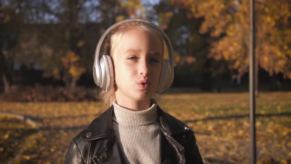 Young Girl in Headphones Listening To Music and Sings Favorite Songs in the Autumn City Park