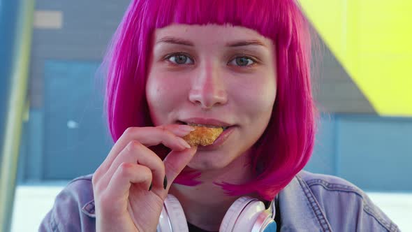 A Young Woman with Pink Hair is Eating Fast Food