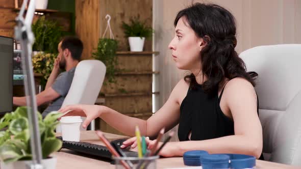 Woman Designer Sips Coffee While Working on the Computer