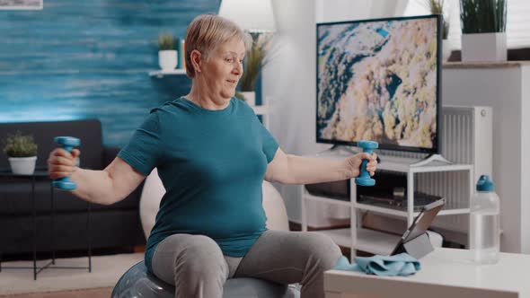 Senior Adult Doing Arm Stretch with Dumbbells on Fitness Toning Ball