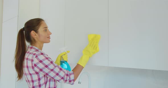 Woman's Hand in a Yellow Rubber Glove Cleans the Shiny Surface of a Modern Plastic Kitchen Cabinet