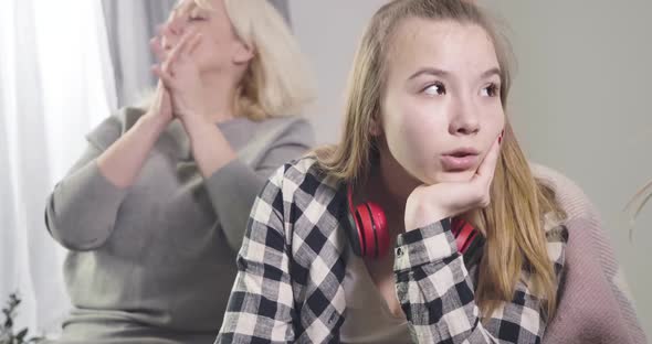 Teen Caucasian Girl Sitting with Irritated Facial Expression As Her Mature Grandmother Shaking Head