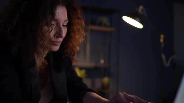 Close Portrait of a Sad Tired Woman at a Work Desk in an Office Late at Night Under the Light of a