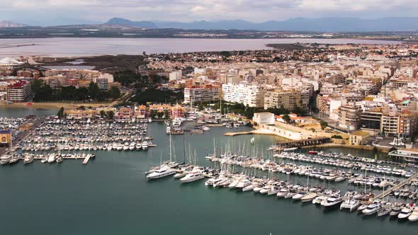 City of Torrevieja buildings and majestic luxury yachts in local pier, aerial side fly view