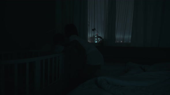 Night Shot of a Mother Waking Up at Night to a Crying Baby in Child Crib