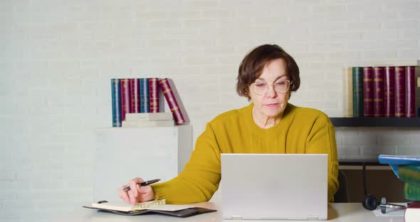An Elderly Caucasian Woman in Glasses Working in Front of a Laptop Monitor She Checks the Report and