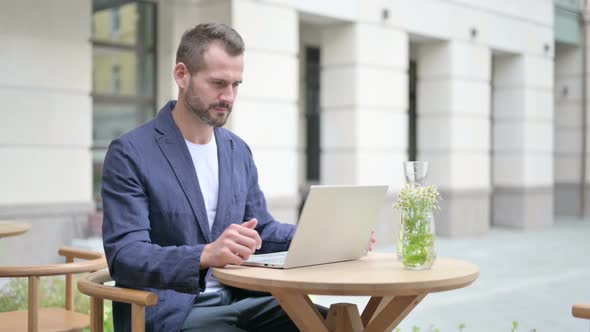 Man Drinking Water While Working on Laptop Sitting in Outdoor Cafe