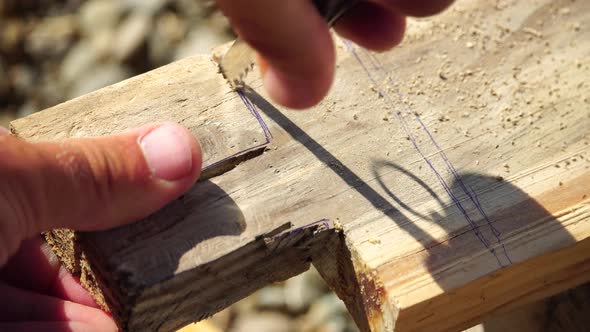 Man Hands Using a Swiss Knife Sawing a Piece of Wood Plank Outdoor Survival and Camping Fun in the