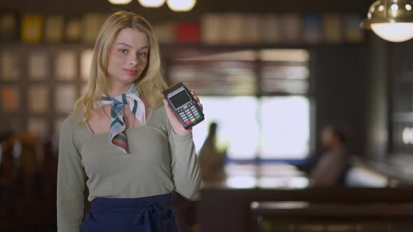 Medium Shot Portrait of Charming Young Waitress Posing with Payment Terminal in Pub Indoors