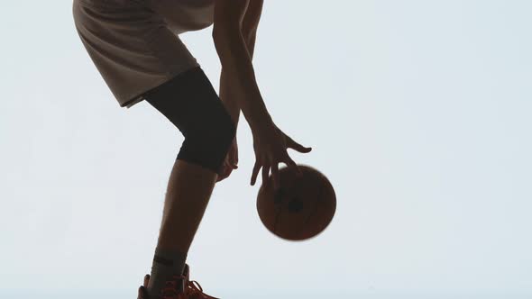 Silhouette of Basketball Player in Sportswear Dribbles Ball Practicing Skills on White Studio