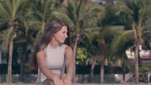 Young Woman in Tight Summer Dressing Against Green Palms