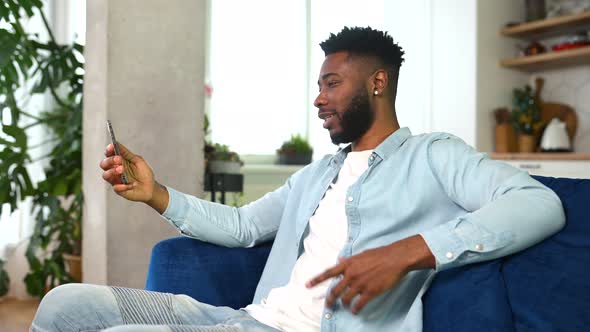 Excited AfricanAmerican Guy with Toothy Smile Using Smartphone for Video Connection