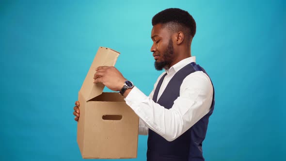 Young African Man Opens Carton Box Dislike What's in It Against Blue Background