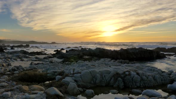 Slow Motion Pacific Ocean Waves Rolling in and Break on a Rocky Coast Under a Sunset Sky at Pacific