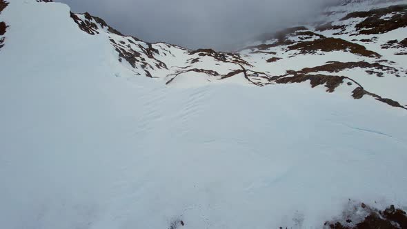 Aerial ascending pedestal birdseye shot of a person laying on snow covered ground and then revealing