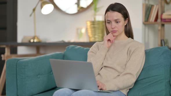 Young Woman with Laptop Thinking on Sofa