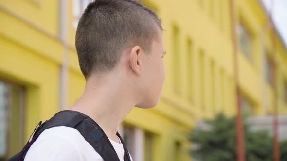 A Caucasian Teenage Boy Looks Around in Thought  Side Closeup  a School in the Background