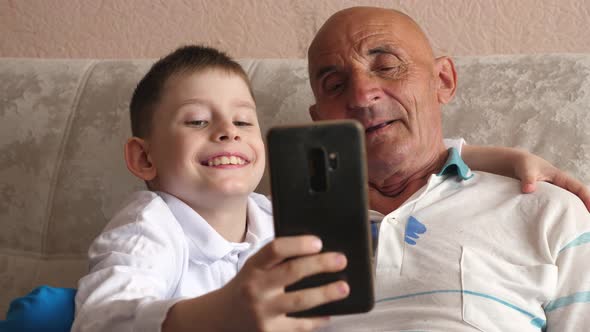 caucasian grandfather 70-79 with a grandson 7-8 years old sitting on the couch posing in front of th