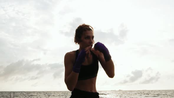 Athletic Young Woman Shadow Boxing By the Sea Against the Sun