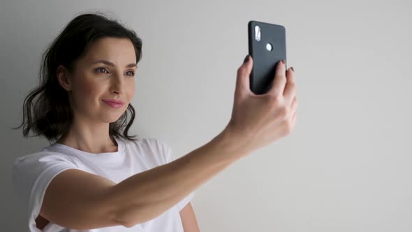 Woman in a White T-shirt on a Light Wall Makes a Selfie