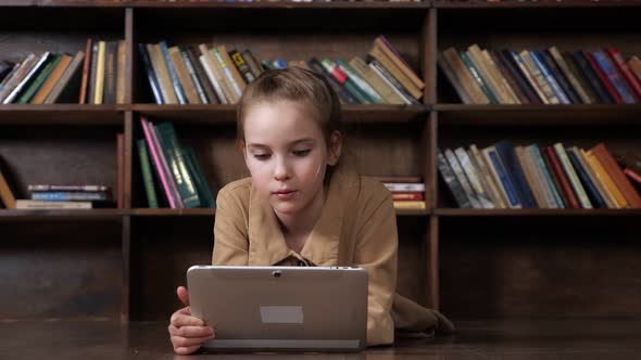 Interested Schoolgirl Plays Online Game on Tablet in Library