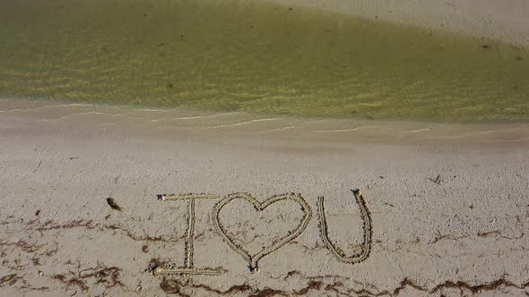 I love U written in the sand as water laps onto the beach.