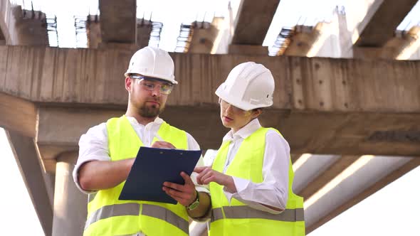 Two Civil Engineers a Young Man and a Young Woman Working on a Project Wearing Safety Helmets are