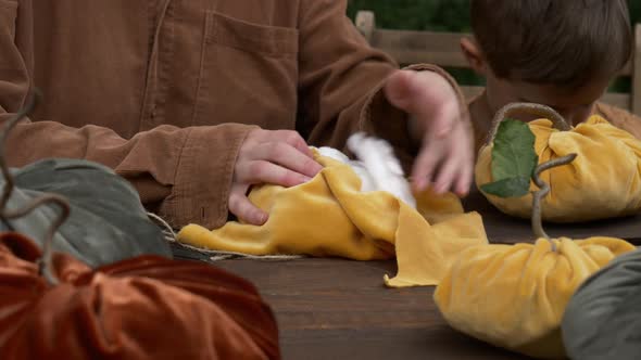 mother with son make pumpkins made of fabric on wooden table in garden