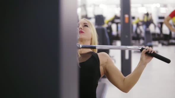 Attractive Young Blond Caucasian Woman with Sporty Body Training Hard on a Lat Pulldown Mashine at