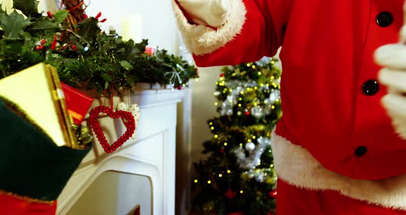 Mid section of santa claus placing gift box on fireplace