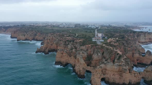 Amazing Aerial Drone View of Lagos Portugal Rocky Coastline with Lighthouse Cloudy Grey Day Circle