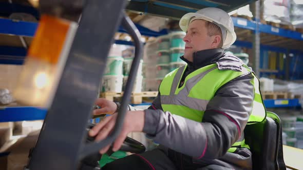 Male Forklift Driver Sitting in Vehicle in Warehouse Indoors