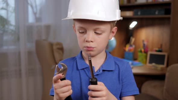 Portrait of a Curious Boy in a Helmet with Various Tools in His Hands at Home