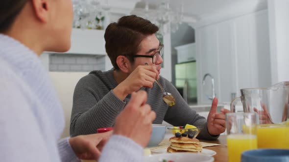 Happy asian parents in kitchen eating breakfast and talking with smiling daughter