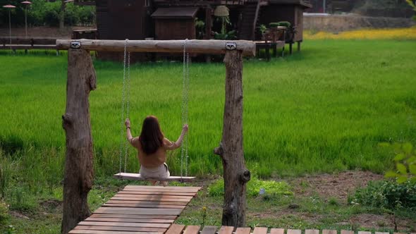 Slow motion of a woman sitting and chilling on wooden swing near by the rice field