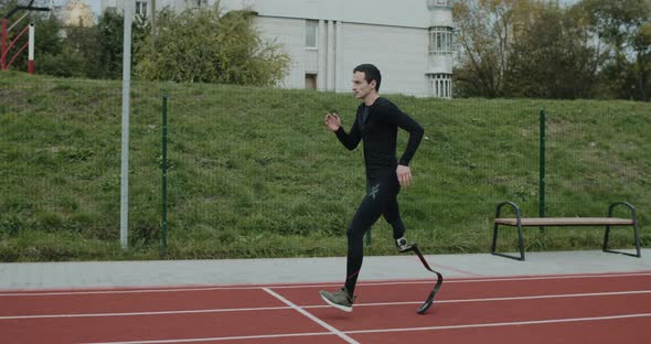 Side View of Disabled Male Sportsman with Amputated Leg with Prosthetic Blade Jogging at Sports