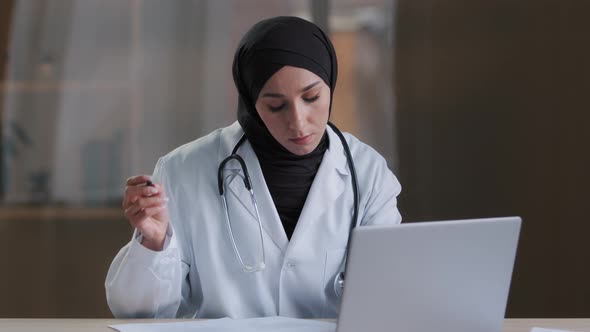 Concentrated Muslim Arabian Female Doctor Chief Physician Practitioner Signs Documents Sit at Clinic